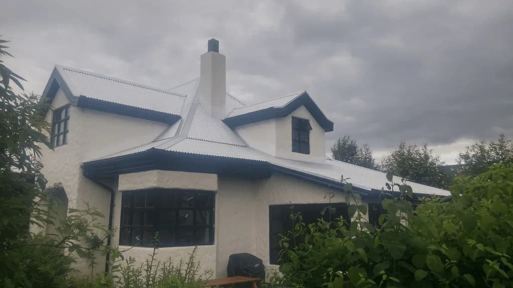 Einbýlishús með ljósu málmþaki, kvisti og hvítum skorsteini.