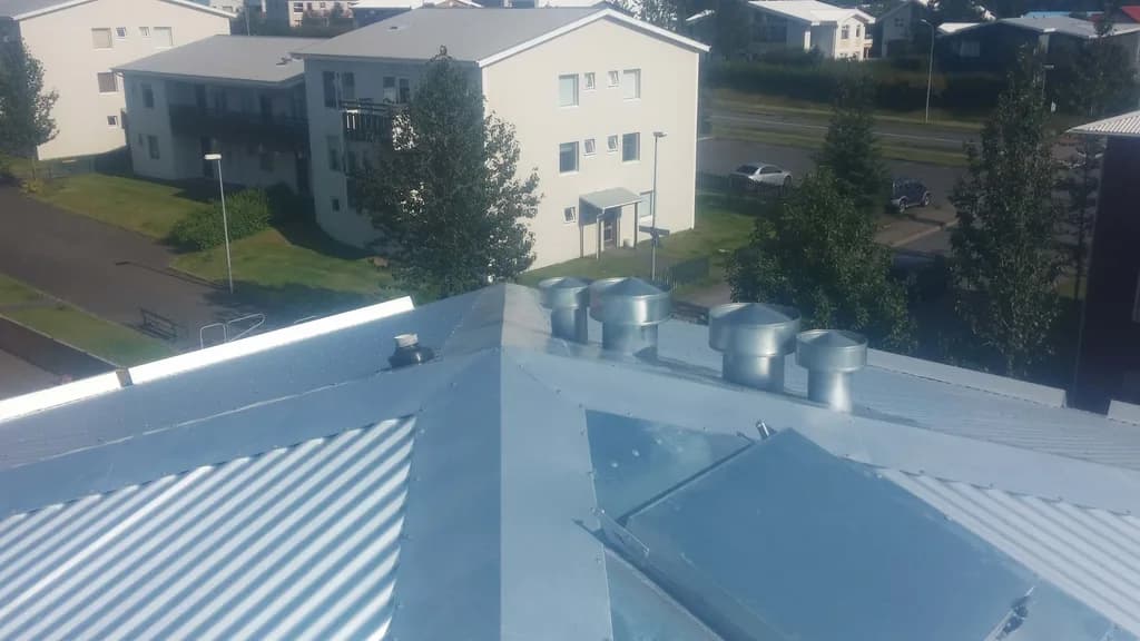 Ljóst báruþak með múruðum skorsteini og loftunartúðum.