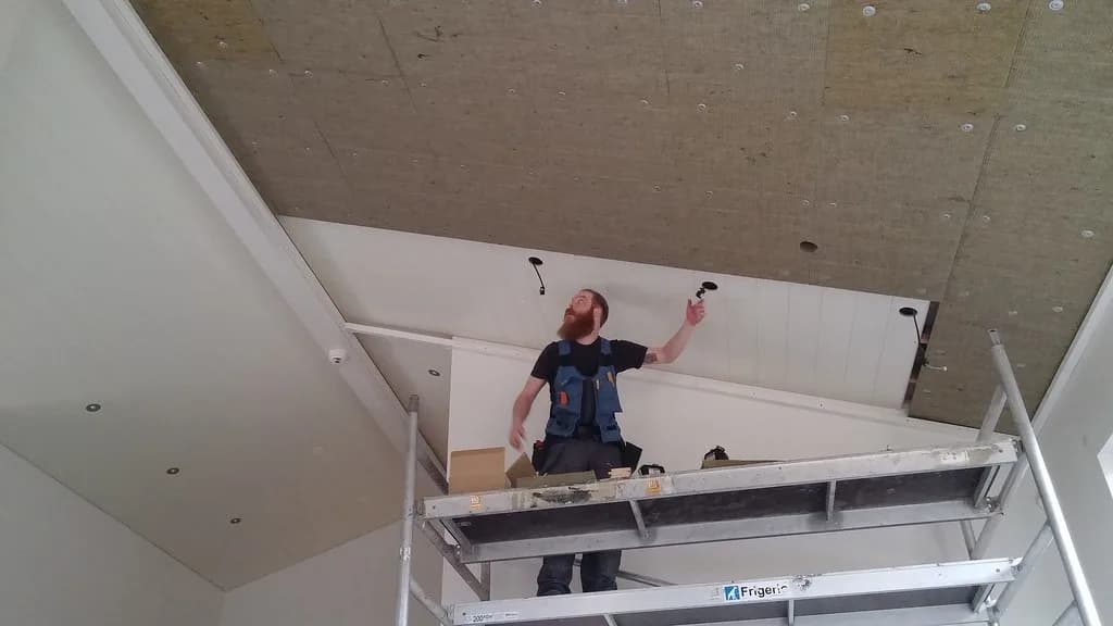 Smiður á vinnupalli við uppsetningu hvíts loftadúks.