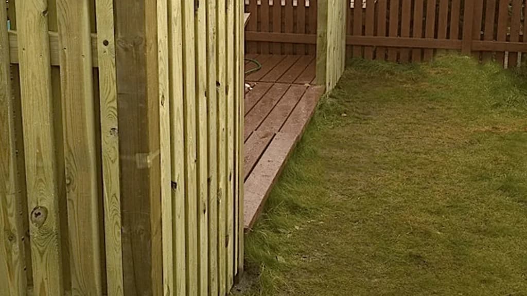Nærmynd af timburskjólvegg við pall og grasflöt.