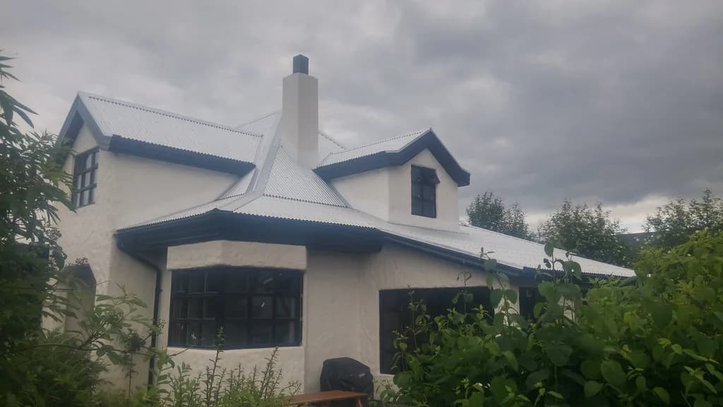 Einbýlishús með ljósu þaki, kvisti og háum hvítum skorsteini.