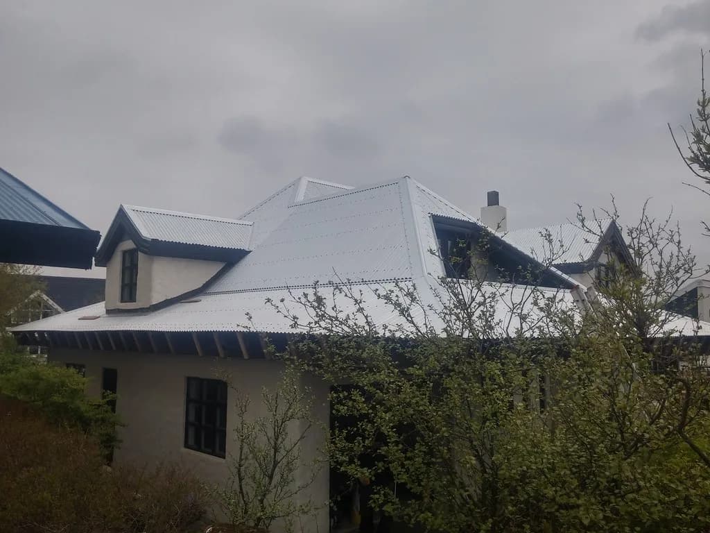 Ljóst málmþak með kvisti og skorsteini á einbýlishúsi.