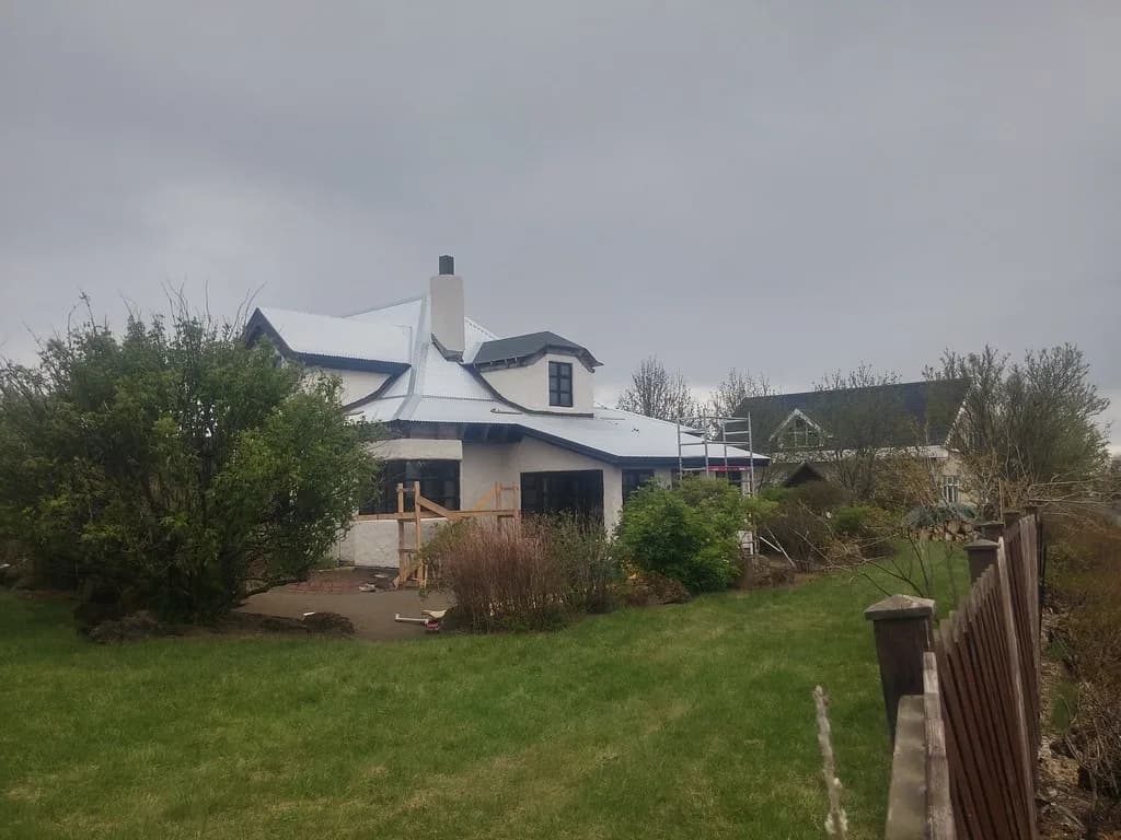 Einbýlishús með ljósu málmþaki, kvistum og garði.