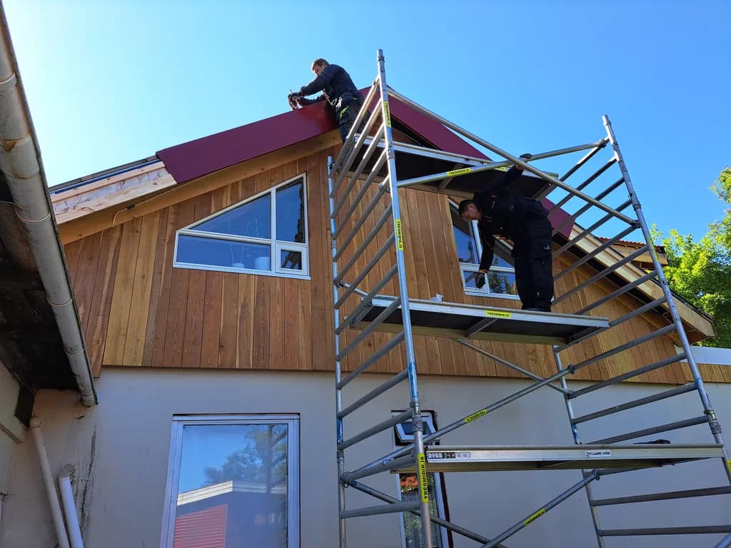 Smiðir á vinnupöllum við þakkant og timburklæddan gafl.
