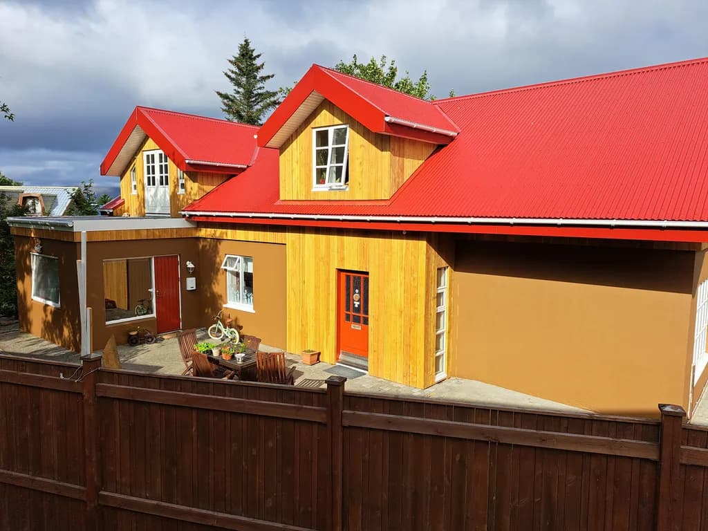 Gult timburhús með rauðu þaki og gluggakvistum.