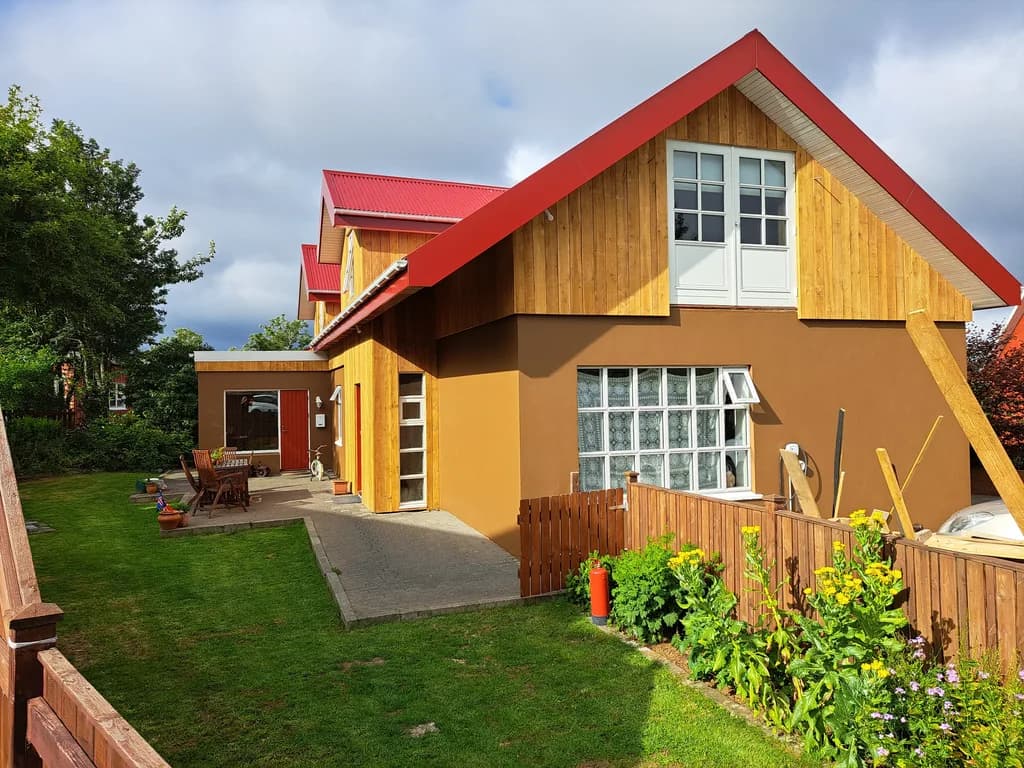 Gult timburhús með rauðu þaki og rauðum þakköntum.