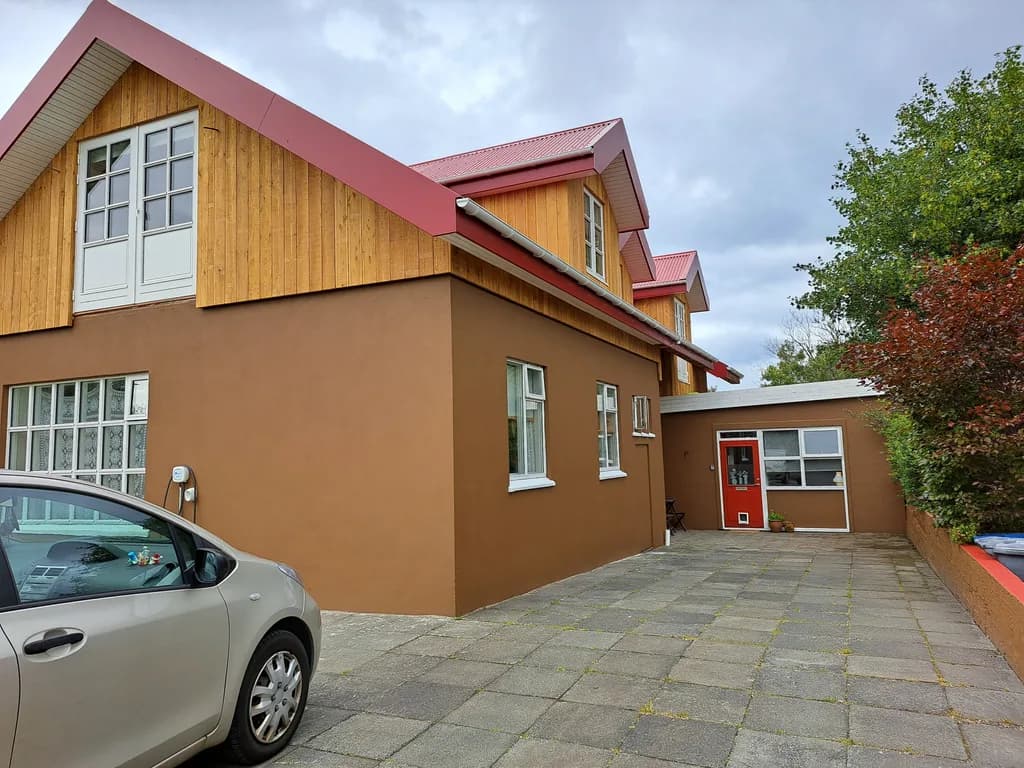 Hús með nýrri timburklæddri hæð, rauðu þaki og kvistum.