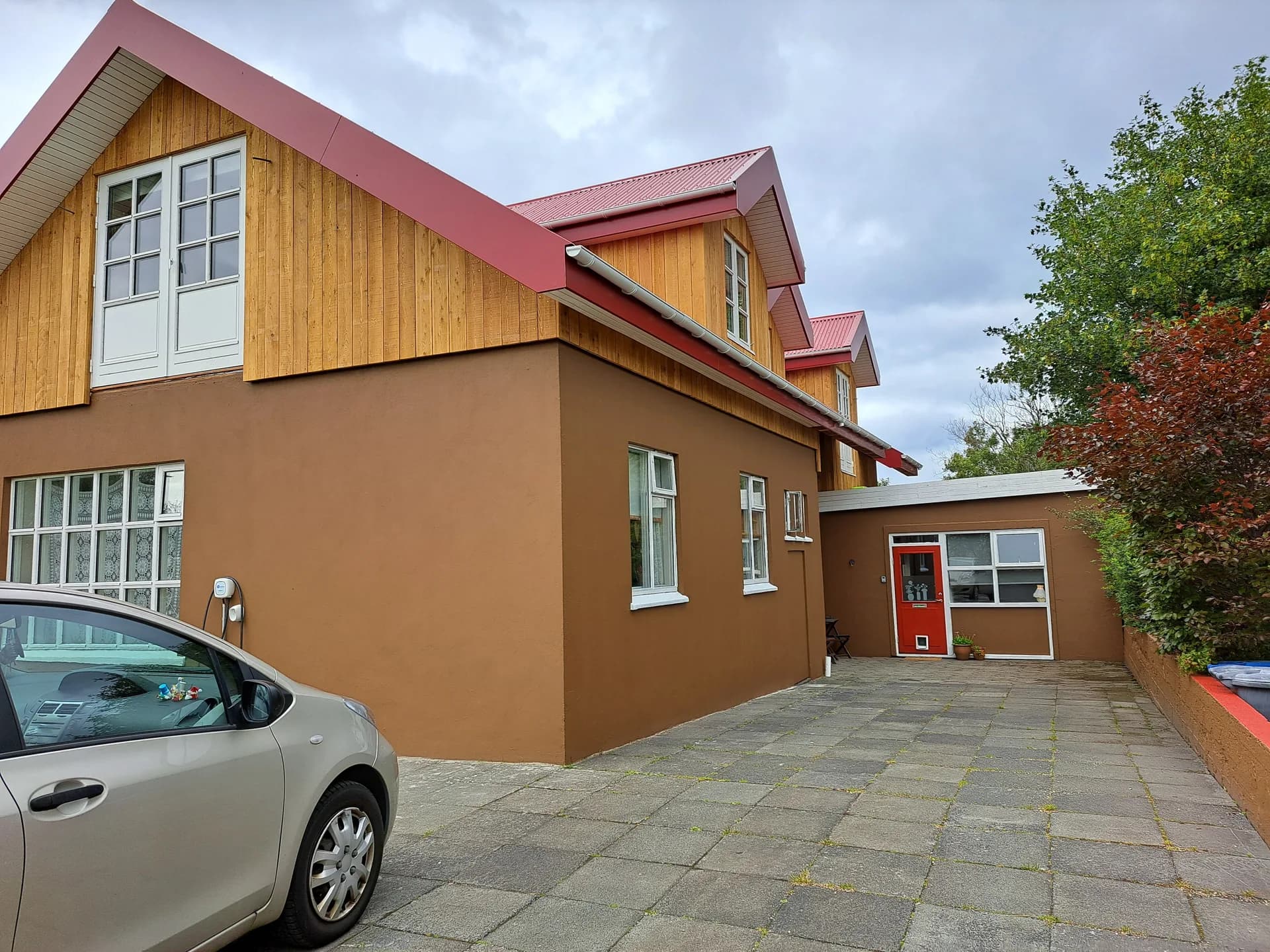 Hús með nýrri timburklæddri hæð, rauðu þaki og kvistum.