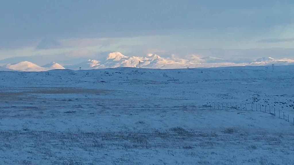 Snævi þakin víðátta með fjöllum í fjarska.