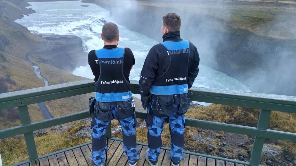 Tveir smiðir í vinnufatnaði horfa yfir Gullfoss.