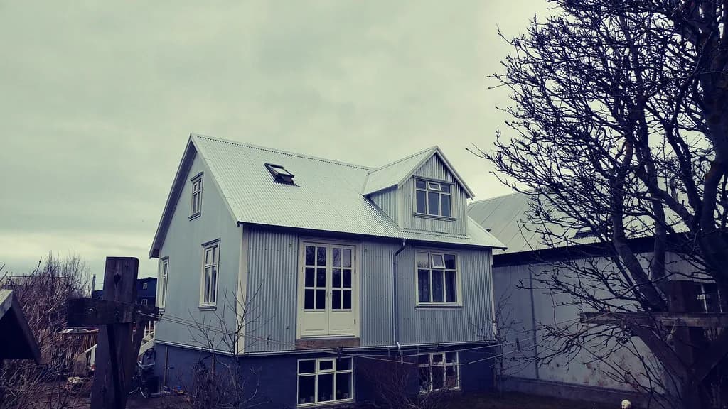 Ljóst báruþak á timburhúsi með kvisti og þakglugga.