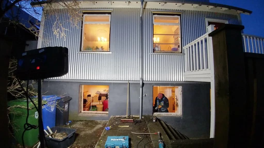 Ný báruð málmklæðning og upplýstir gluggar á húsvegg.