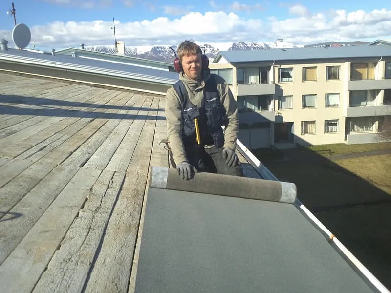Smiður við opið timburþak og þakbrún.