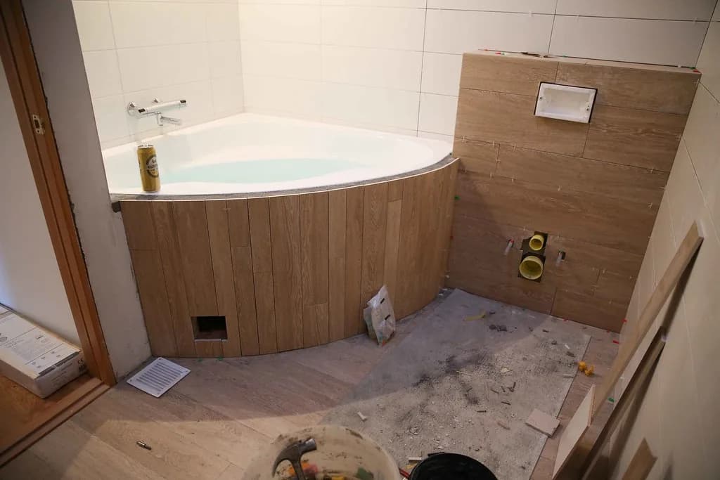 Hornbaðkar með viðarklæðningu og flísum við vegg.