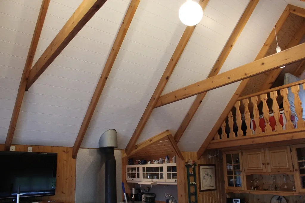 Frágengið hvítt loft með timbursperrum ofan við arin.