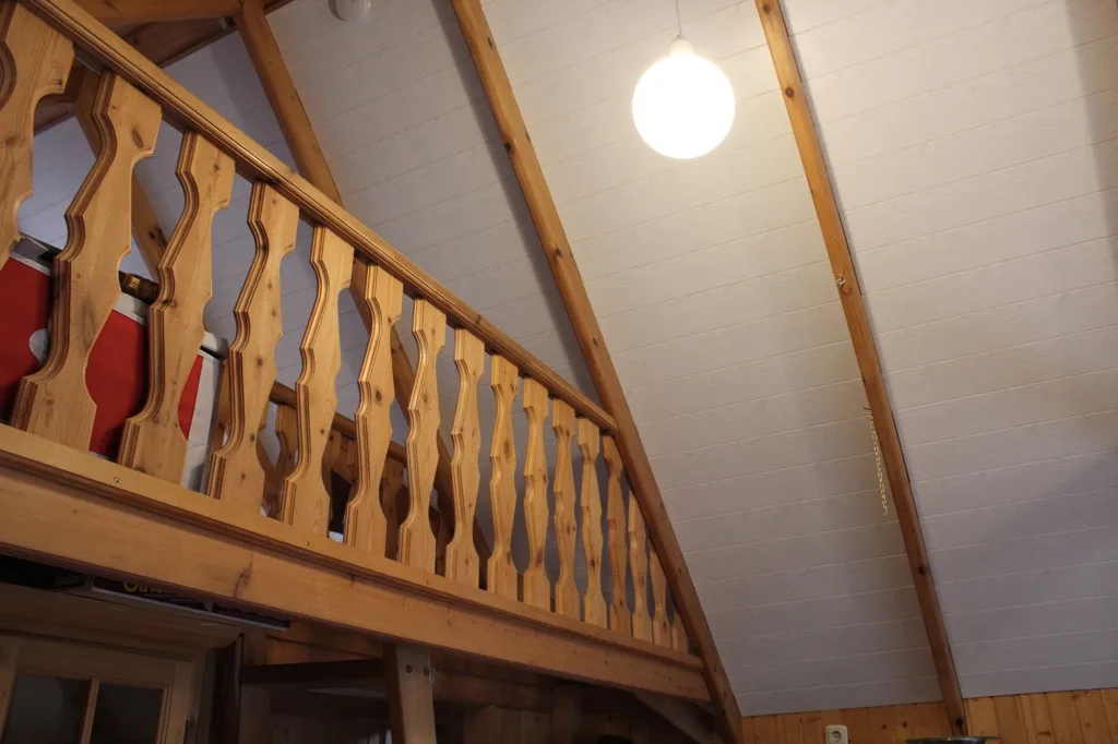 Svefnloft með timburhandriði og hvítri klæðningu í lofti.