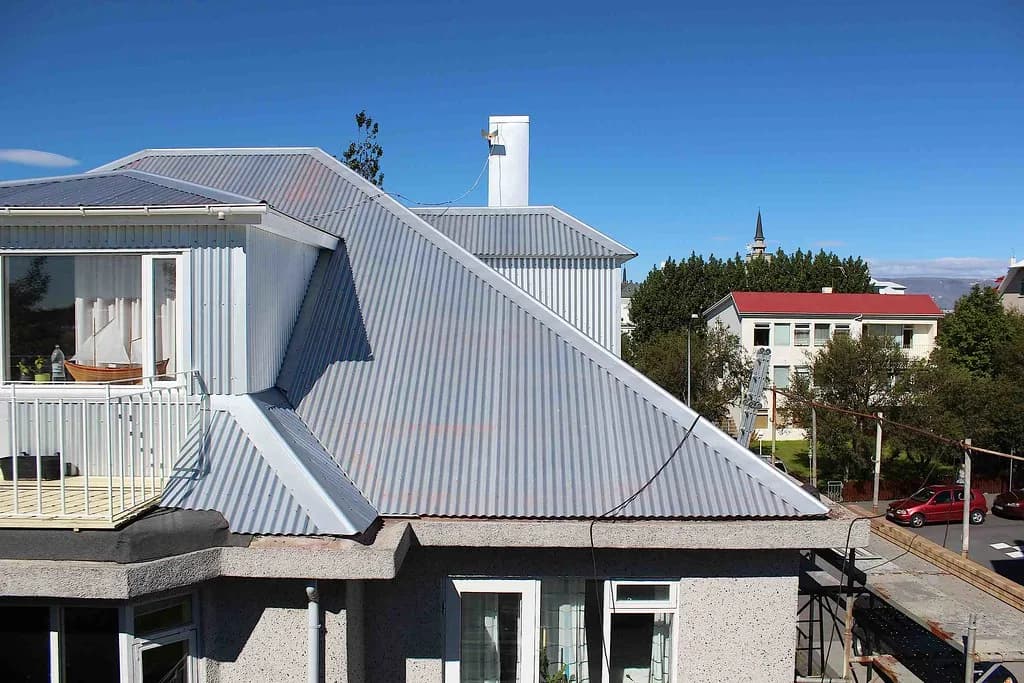 Ljóst báruþak með gluggakvisti og hvítum skorsteini.