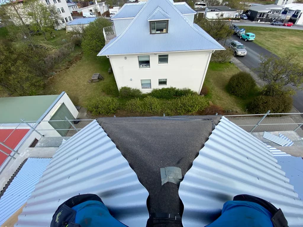 Smiður situr á ljósu báruþaki yfir þakdal.