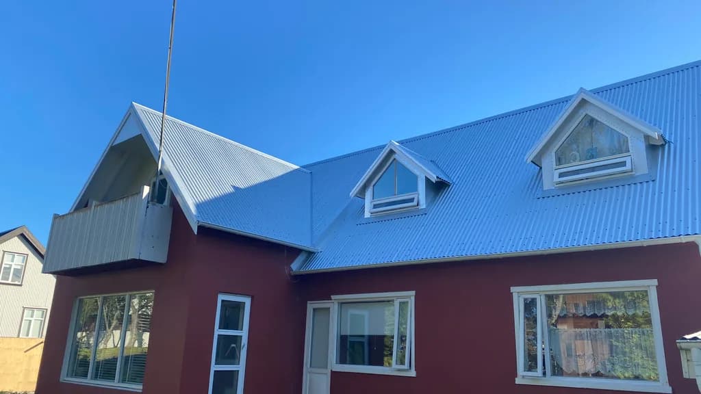 Rautt hús með ljósu málmþaki og litlum kvistum.