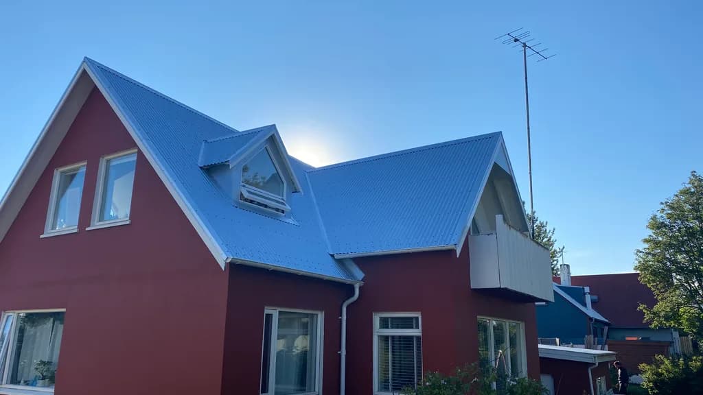 Ljóst báruþak og gluggakvistur á rauðu húsi.