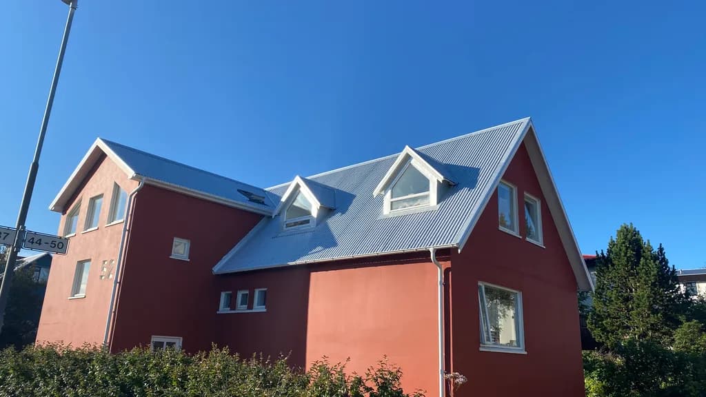 Rautt hús með tveimur gluggakvistum og nýju ljósu málmþaki.