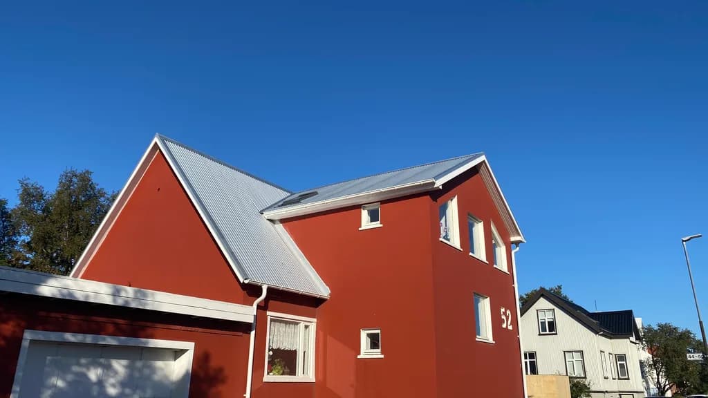 Rautt hús með nýrri ljósri málmþakklæðningu.