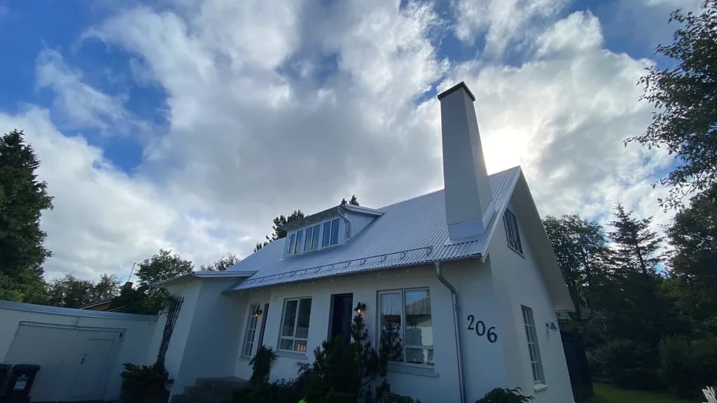 Ljóst málmþak með kvistum og háum skorsteini á hvítu húsi.