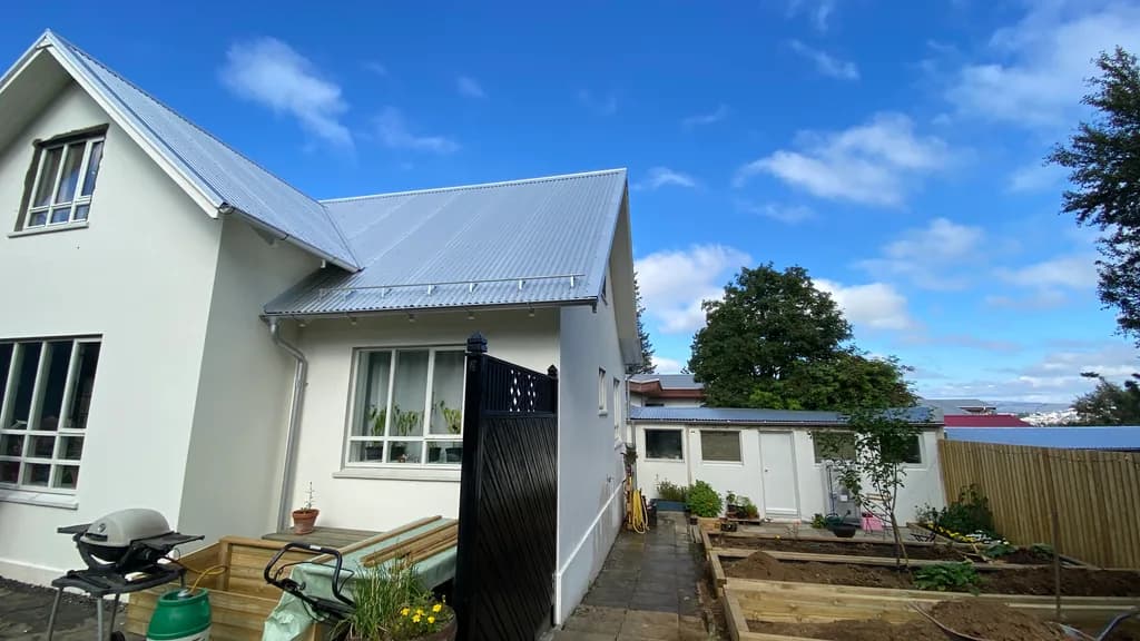 Hvítur húsveggur með glugga undir nýju ljósu þaki.