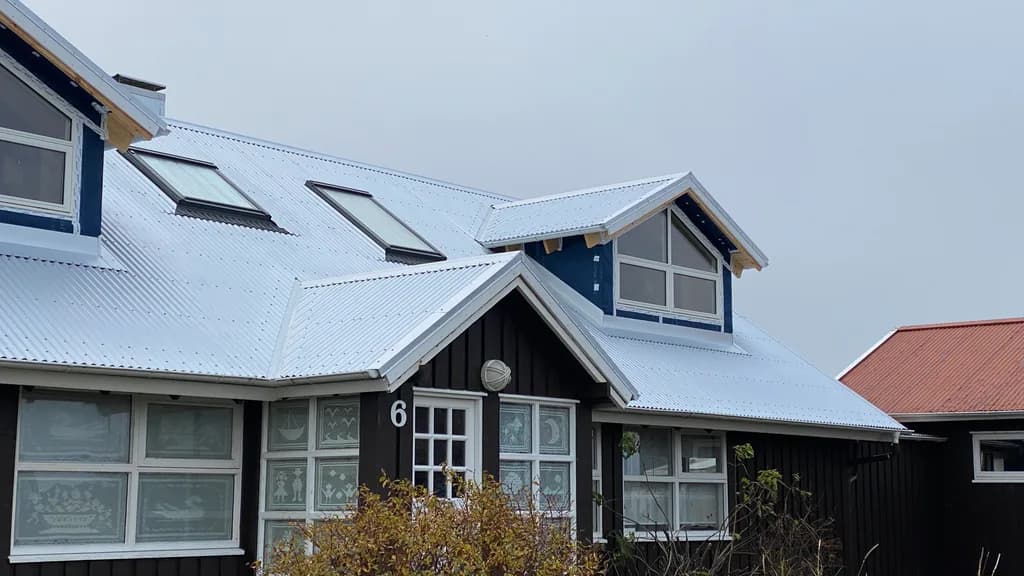 Dökkt timburhús með nýju ljósu báruþaki og gaflkvistum.