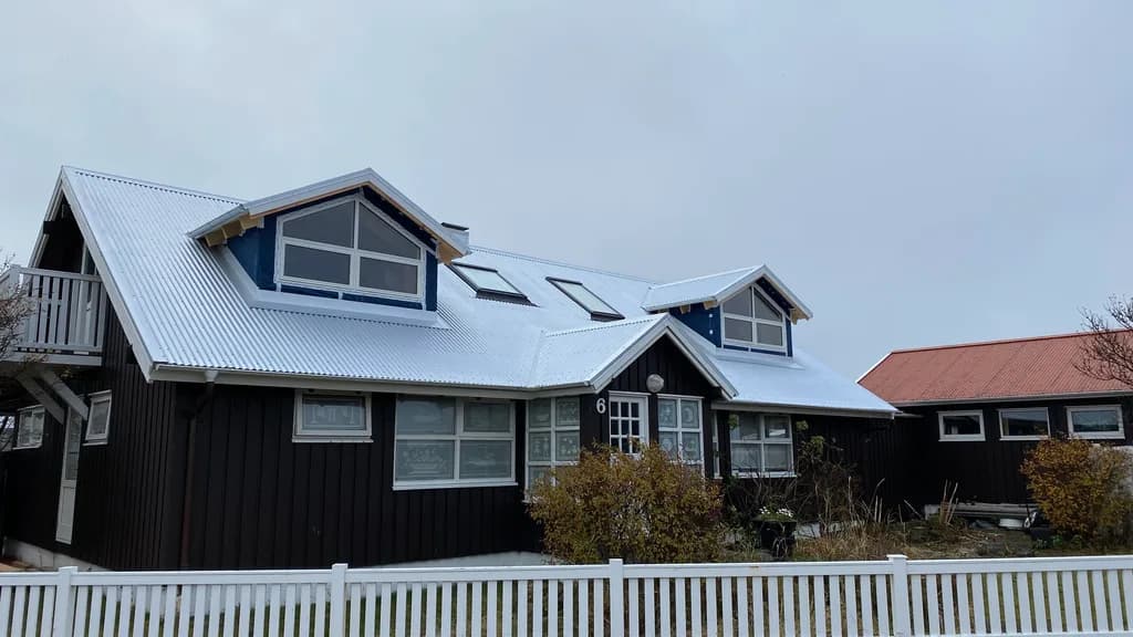 Ljóst þak með tveimur gaflkvistum og þakgluggum á dökku timburhúsi.