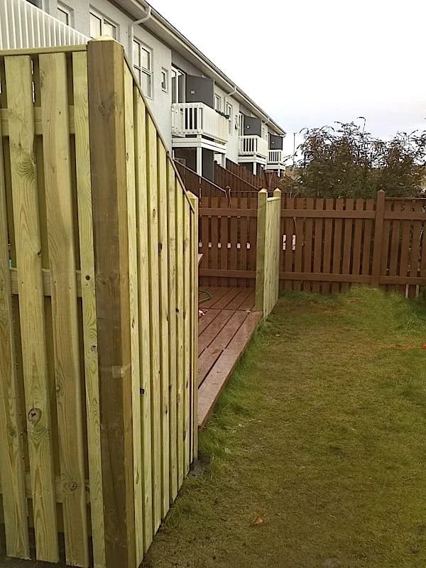 Timburskjólveggur við pall og grasflöt.