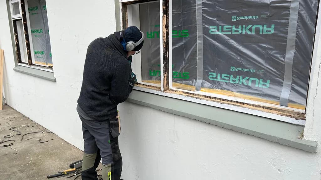 Smiður vinnur að gluggaviðgerð utan á húsi með gluggana hulda plasti