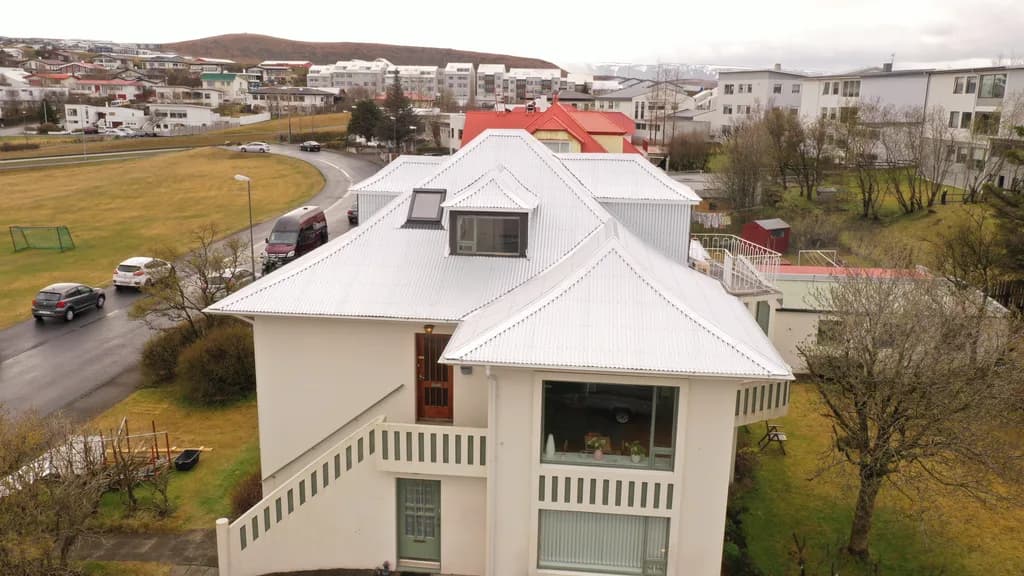 Loftmynd af húsi með ljósu málmþaki og kvistum.